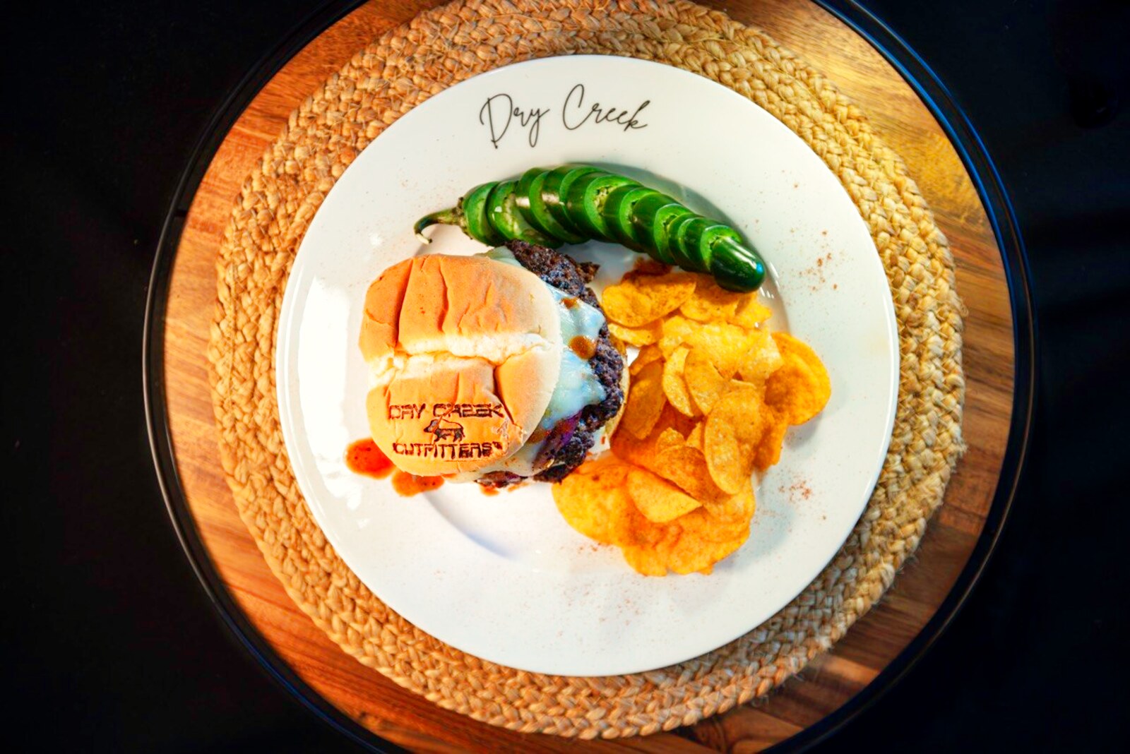 A branded burger plated with jalapeno and chips
